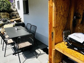 Eine Terrasse im Freien mit Tisch, Stühlen, einem Grill und einer Steinwand mit Pflanzen.
