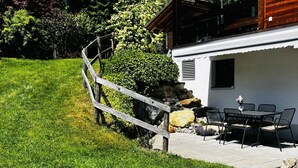 Eine Terrasse mit Gartenmöbeln, einem Holzzaun und einem Gebäude mit einem Fenster.