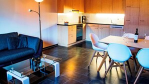 Ein modernes Interieur mit einer Couch, einem Couchtisch, einem Esstisch mit Stühlen und Küchenschränken aus Holz.