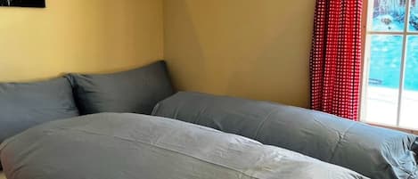Una habitación con una cama, un ventanal con cortinas rojas y un cuadro en la pared.