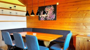 A restaurant with a wooden interior, a long table with blue chairs, and pendant lighting. - HasliRent, Eiger, (Hasliberg Reuti), by Interhome (Hasliberg)