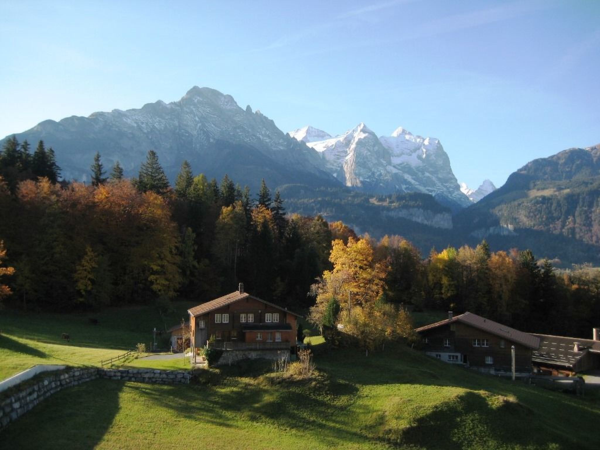 A mountain landscape with two wooden buildings, one with a balcony and a stone wall in the foreground.