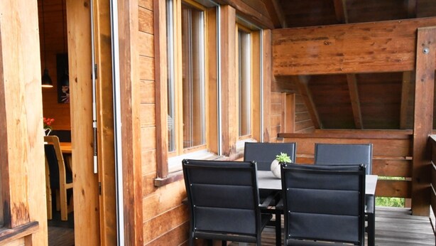 A wooden deck with a table and chairs, large windows, and a view of the outdoors. - HasliRent, Eiger, (Hasliberg Reuti), by Interhome (Hasliberg)