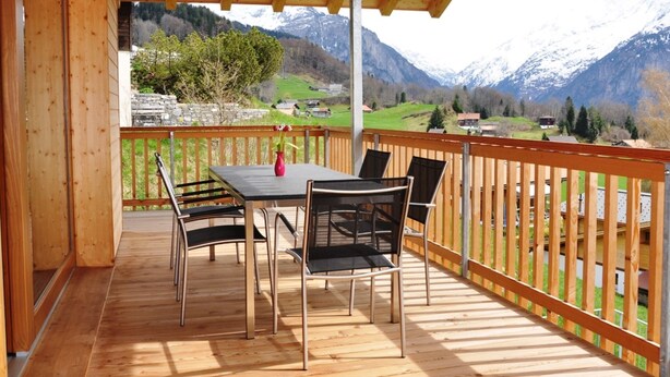 Une terrasse en bois avec une table et des chaises, offrant une vue sur un paysage montagneux.
