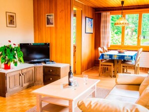 A cozy living room with a sofa, a television, a dining table with chairs, and a window with a view of greenery. - HasliRent, Resti, (Hasliberg Reuti), by Interhome (Hasliberg)