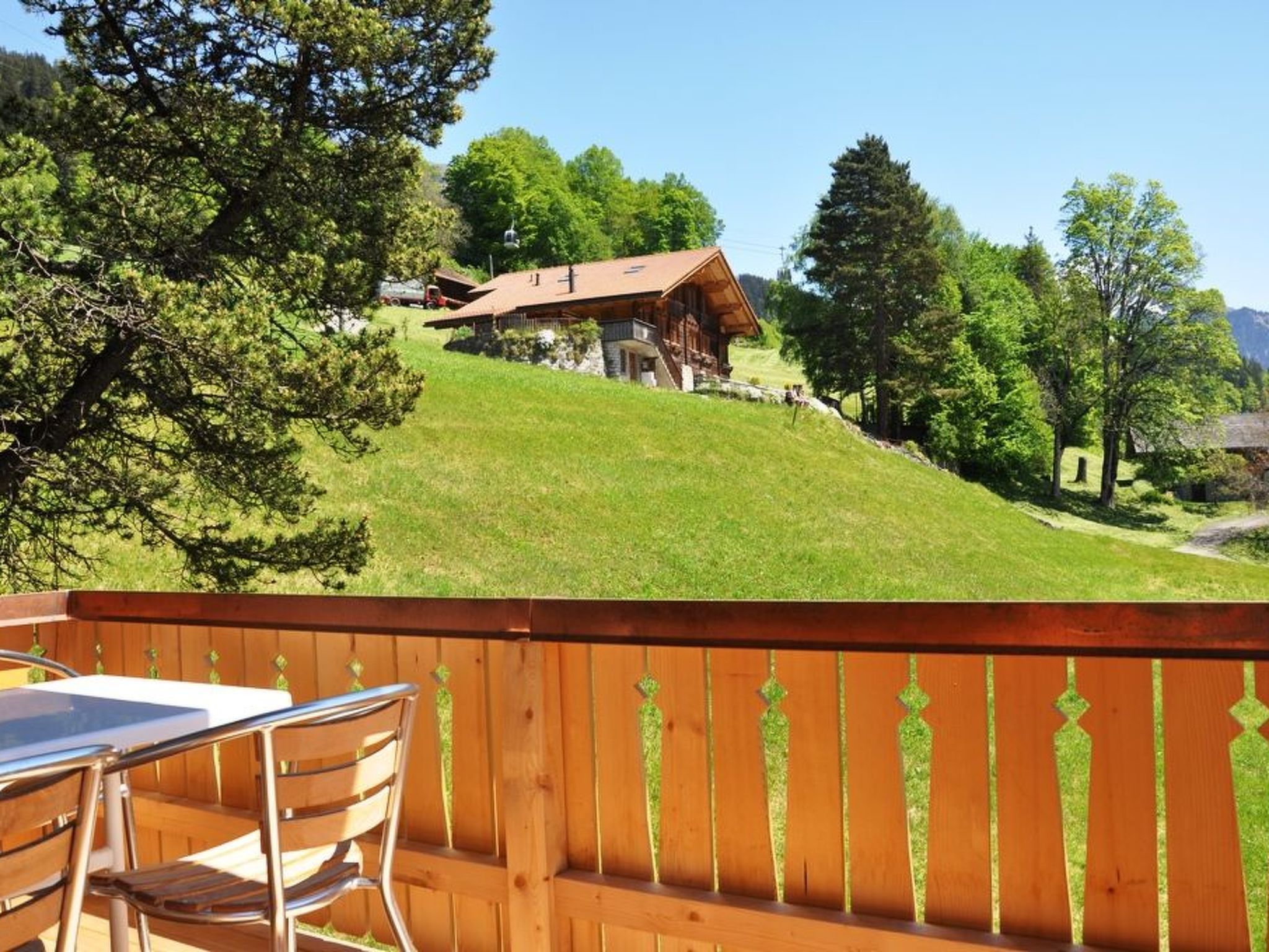 Eine Holzterrasse mit Tisch und Stühlen mit Blick auf einen grasbewachsenen Hügel und eine Holzhütte.