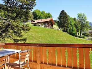 A wooden deck with a table and chairs, overlooking a grassy hill with a wooden cabin. - HasliRent, Resti, (Hasliberg Reuti), by Interhome (Hasliberg)