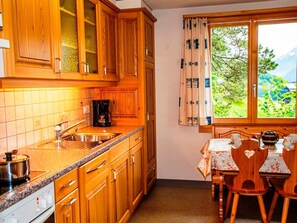 A kitchen with wooden cabinets, a sink, a coffee maker, and a dining area with a table and chairs. - HasliRent, Resti, (Hasliberg Reuti), by Interhome (Hasliberg)