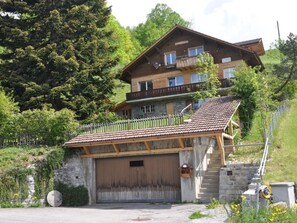 A two-story wooden chalet with a balcony, a stone garage, and a hillside backdrop. - HasliRent, Resti, (Hasliberg Reuti), by Interhome (Hasliberg)