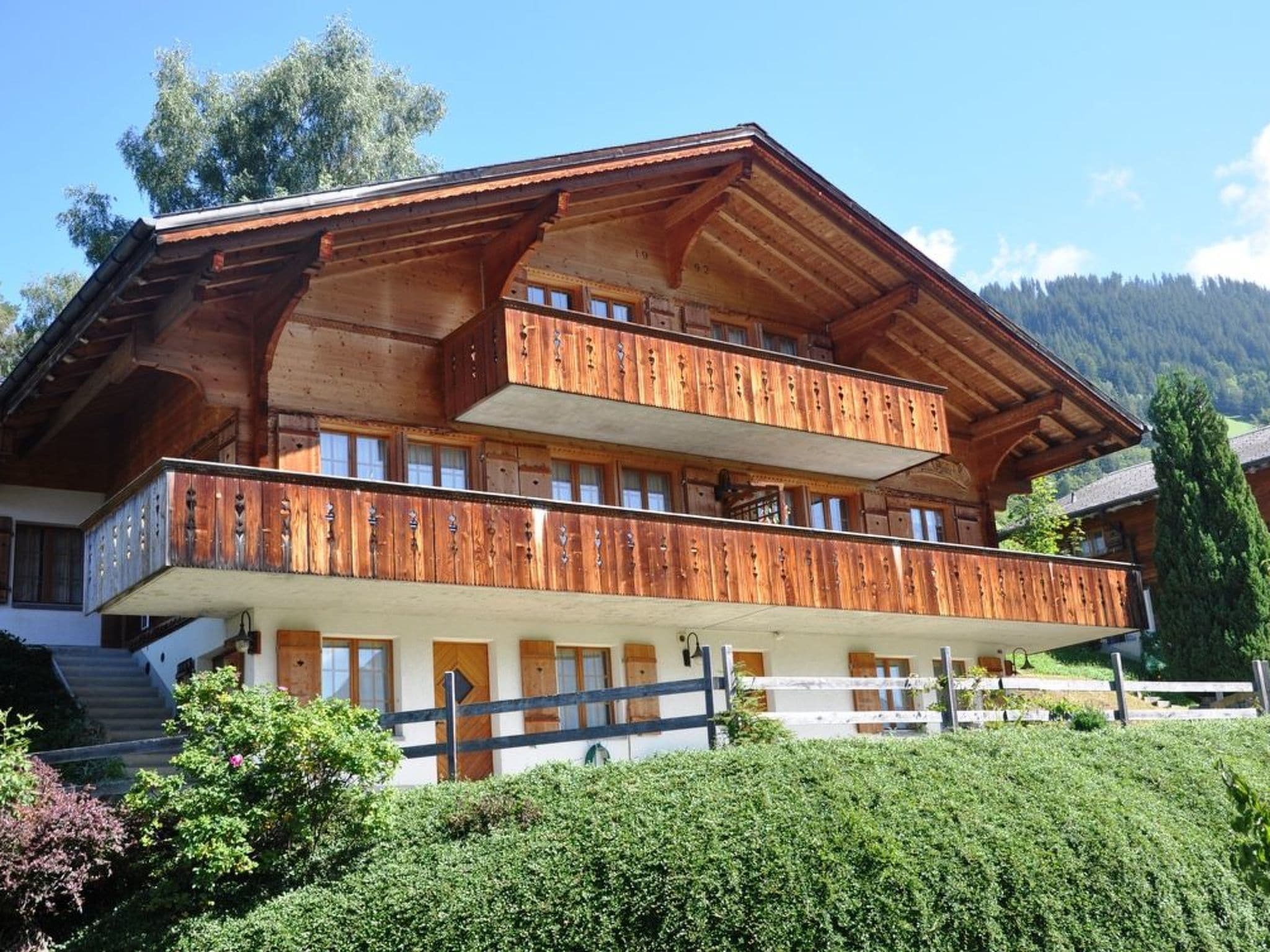 Eine mehrstöckige Holzhütte mit Balkonen, einer weißen Fassade und einer Bergkulisse.