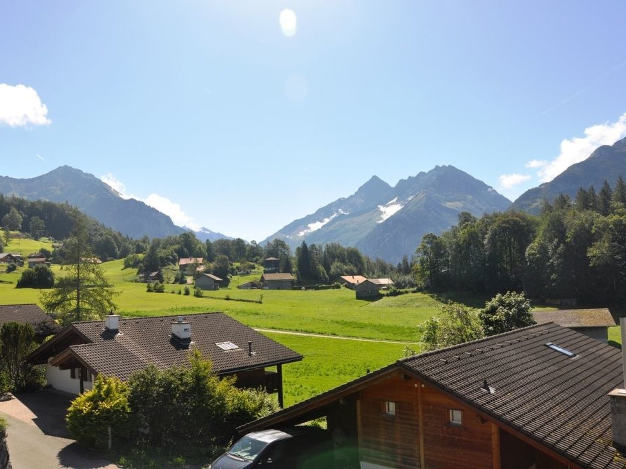 A rural village with houses, green fields, and mountains in the background.