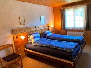 A double bed with a headboard, bedside lamps, and a window with curtains. - HasliRent, Wetterhornblick, (Hasliberg Reuti), by Interhome (Hasliberg)