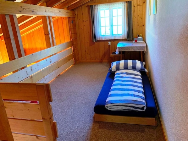 A small, cozy room with a bunk bed, a single bed, a desk, and a window.