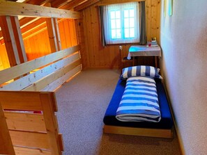 Una habitació petita i acollidora amb literes, un llit individual, un escriptori i una finestra.