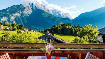 Une table avec des chaises et un vase de fleurs, donnant sur un paysage montagneux parsemé de maisons et de verdure.