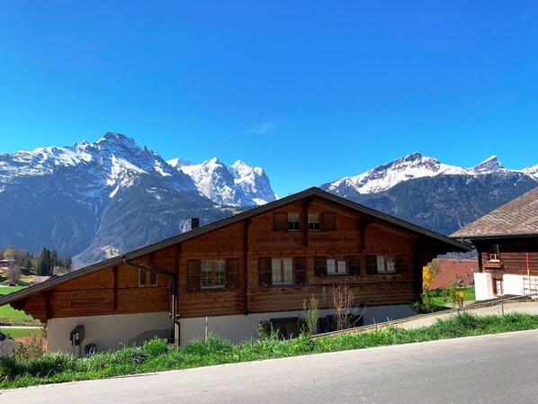 Una xalet de fusta amb teulada inclinada, situada davant d'unes muntanyes nevades sota un cel blau clar.