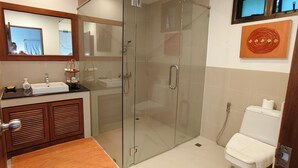 A bathroom with a glass-enclosed shower, a sink with toiletries, and a toilet. - Deluxe Room No. 2 with Ocean View (Sakhu)