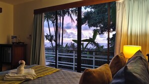 A hotel room with a bed, a desk, a lamp, and a view of the ocean. - Deluxe Room No. 2 with Ocean View (Sakhu)