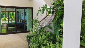 A room with a sliding glass door leading to a balcony, a staircase, and lush greenery. - Deluxe Room No. 2 with Ocean View (Sakhu)