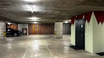 Un parking avec des planchers en béton, une voiture garée dans une place et une porte ornée d’un motif rouge et blanc sur le mur.