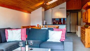 Un salon moderne avec un canapé et une table basse, une cuisine en arrière-plan et des poutres en bois au plafond.