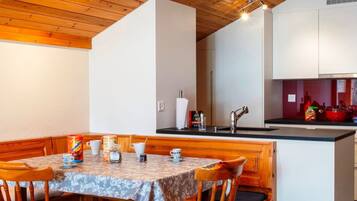 Un coin repas avec une table et des chaises en bois, une cuisine avec des meubles blancs et un plafond en bois.