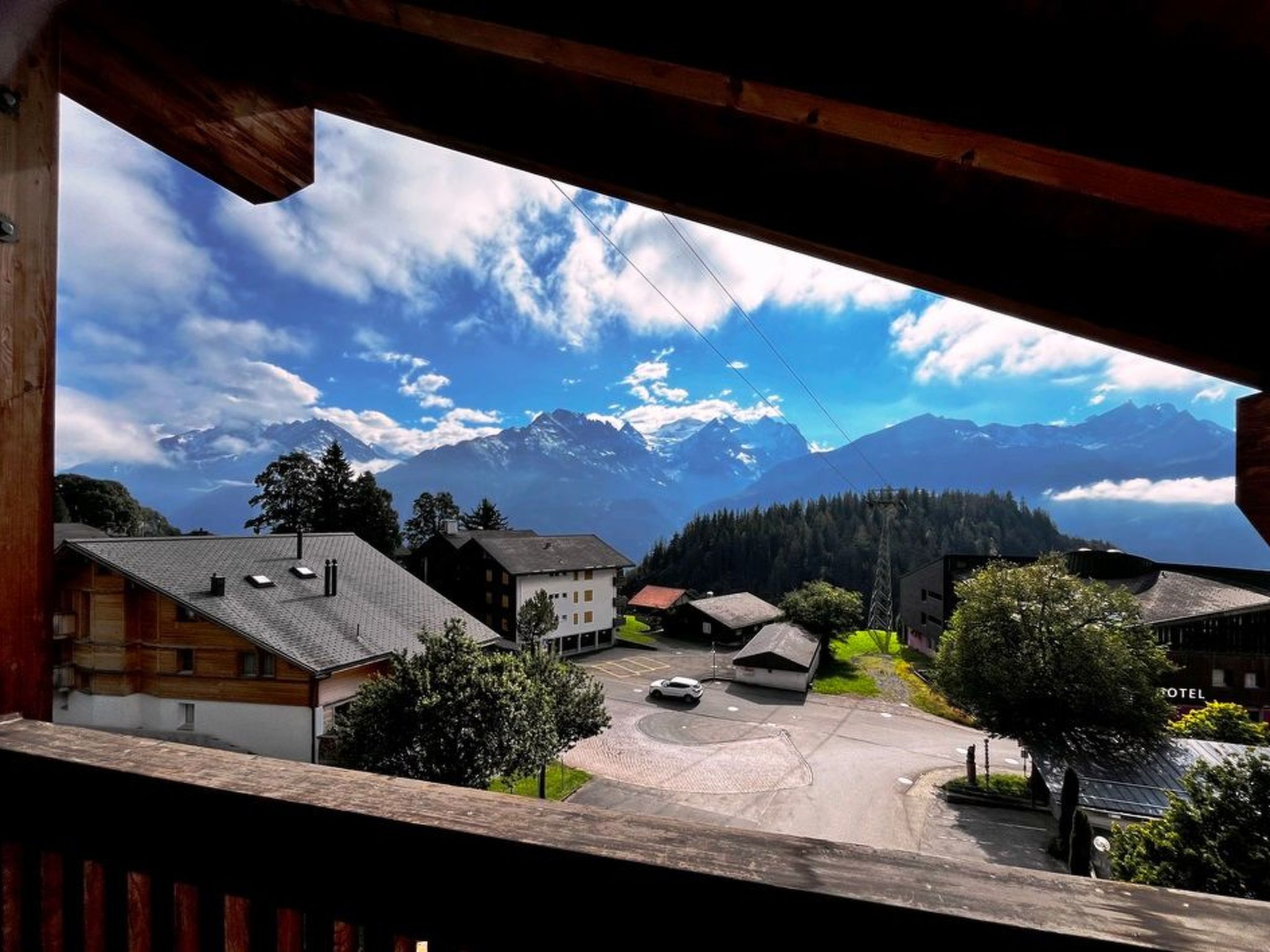 A view of a mountain village with traditional buildings, a clear sky, and a road leading to a hotel.