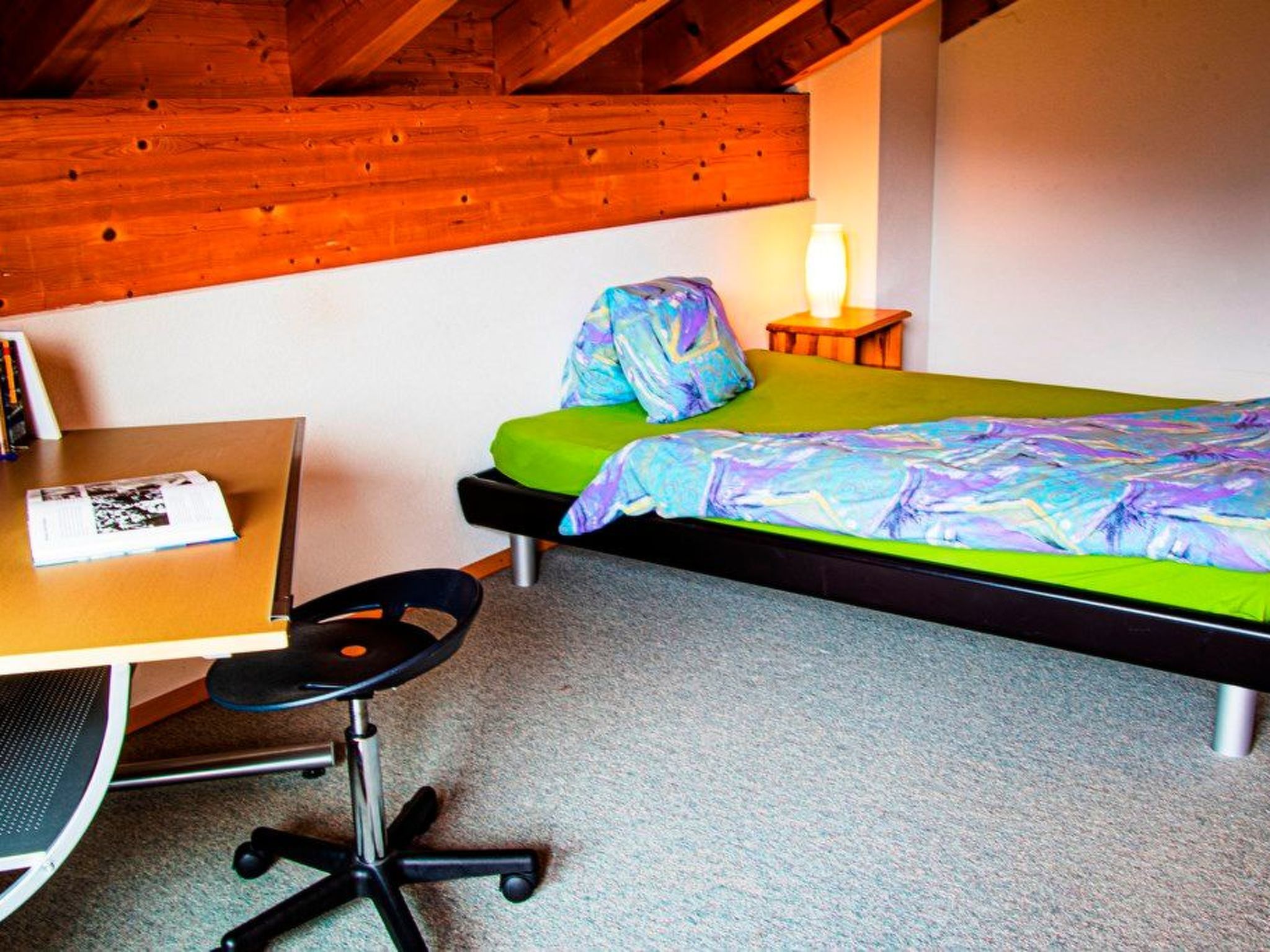 A small room with a single bed, a desk, and a chair.