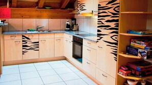 Une cuisine avec des meubles de rangement en bois, un four encastré et une étagère remplie de jeux de société.