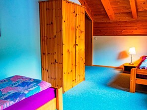 Ein Zimmer mit einem Bett, einem Kleiderschrank, einem Nachttisch mit Lampe und einem blauen Teppich.