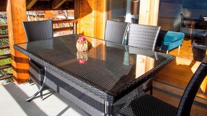 Une table à plateau en verre, des chaises en osier, un vase rempli de fleurs et une vue sur l’extérieur.