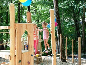 A wooden play structure in a wooded area with climbing elements and ropes. - HasliRent, Schrotenweidli, (Hasliberg Hohfluh), by Interhome (Hasliberg)