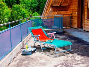 A wooden building with a balcony, a metal railing, and two lounge chairs with cushions.