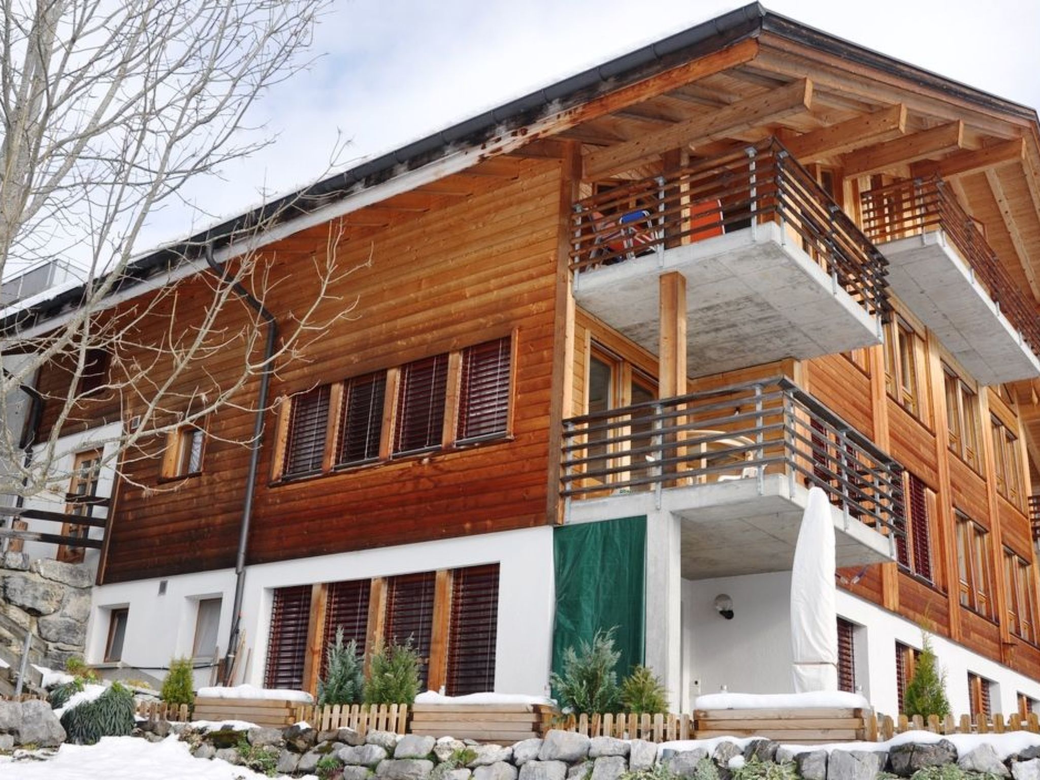 A multi-story wooden building with balconies, a stone foundation, and a snow-covered ground.