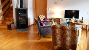 Un salon avec une cheminée, des fauteuils à motifs, un téléviseur et un escalier en bois.