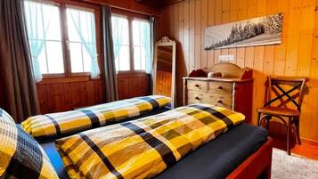 Une chambre avec deux lits, une commode, une chaise et un tableau au mur.