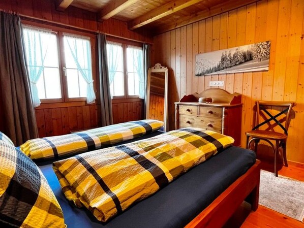 A room with two beds, a dresser, a chair, and a painting on the wall. - HasliRent, Cosy 2, (Hasliberg Wasserwendi), by Interhome (Hasliberg)