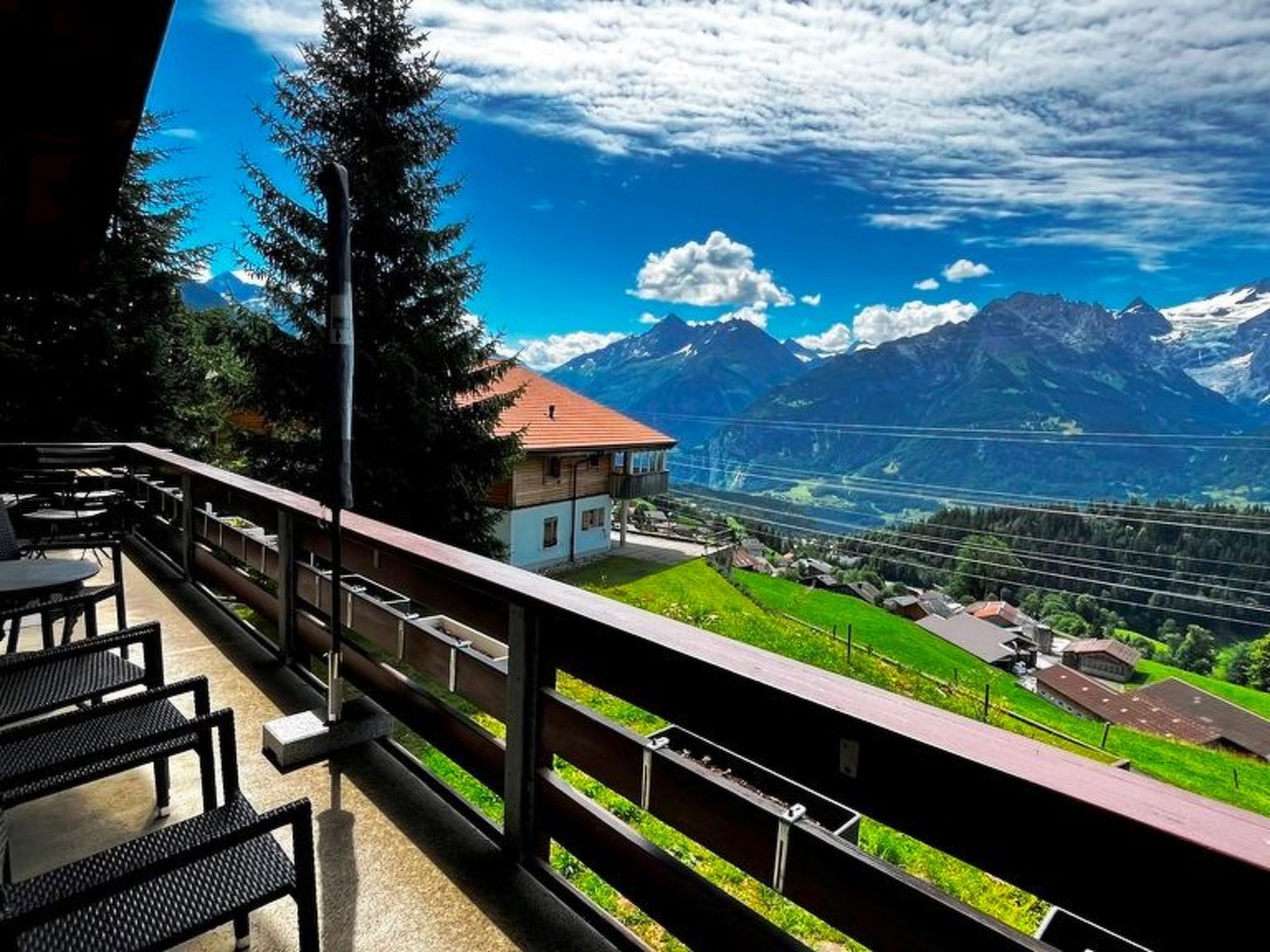 Ein Balkon mit Sitzgelegenheit und Blick auf eine gebirgige Landschaft unter blauem Himmel.