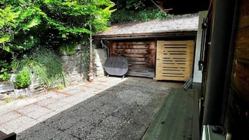 Un garage avec une porte en bois, un sol en béton et une allée en gravier menant à un véhicule garé.