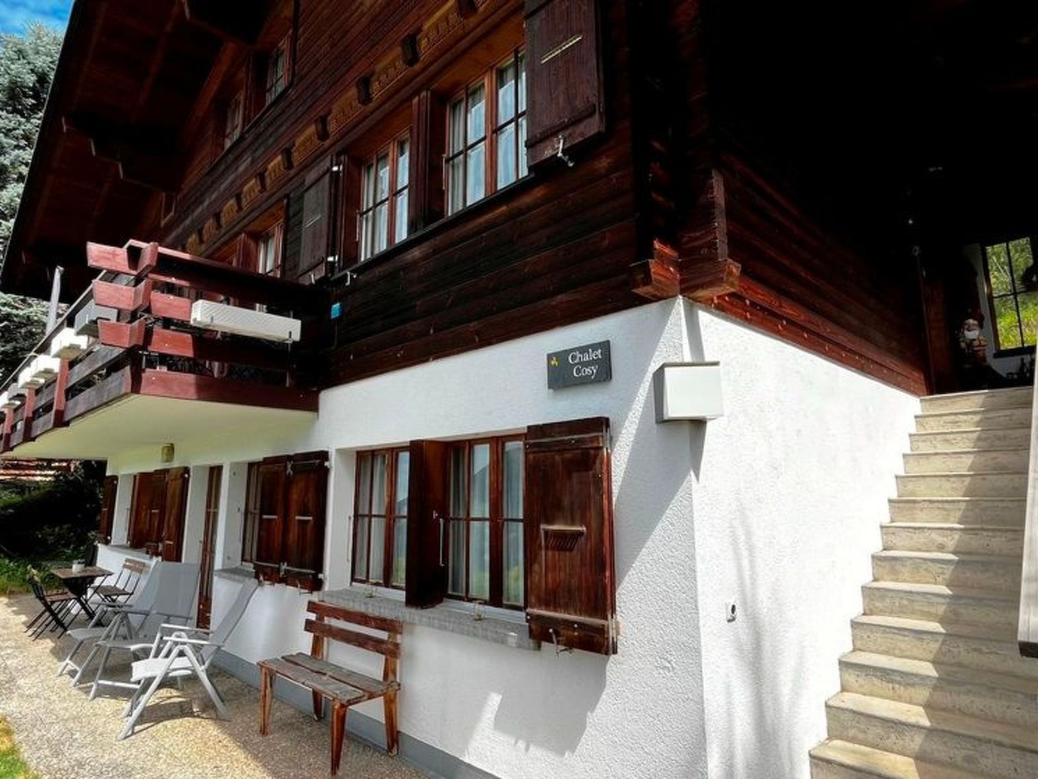 Un chalet à la façade blanche, aux volets en bois et doté d’un balcon avec une balustrade en bois.