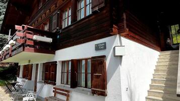 Un chalet à la façade blanche, aux volets en bois et doté d’un balcon avec une balustrade en bois.