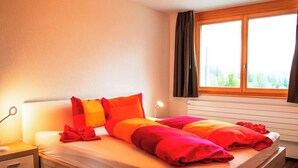 Une chambre à coucher avec un lit, des tables de chevet, une fenêtre avec des rideaux et une vue sur la verdure à l’extérieur.