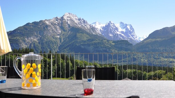 Une table avec un pichet en verre transparent et un verre, une chaise en métal et une vue sur la montagne.
