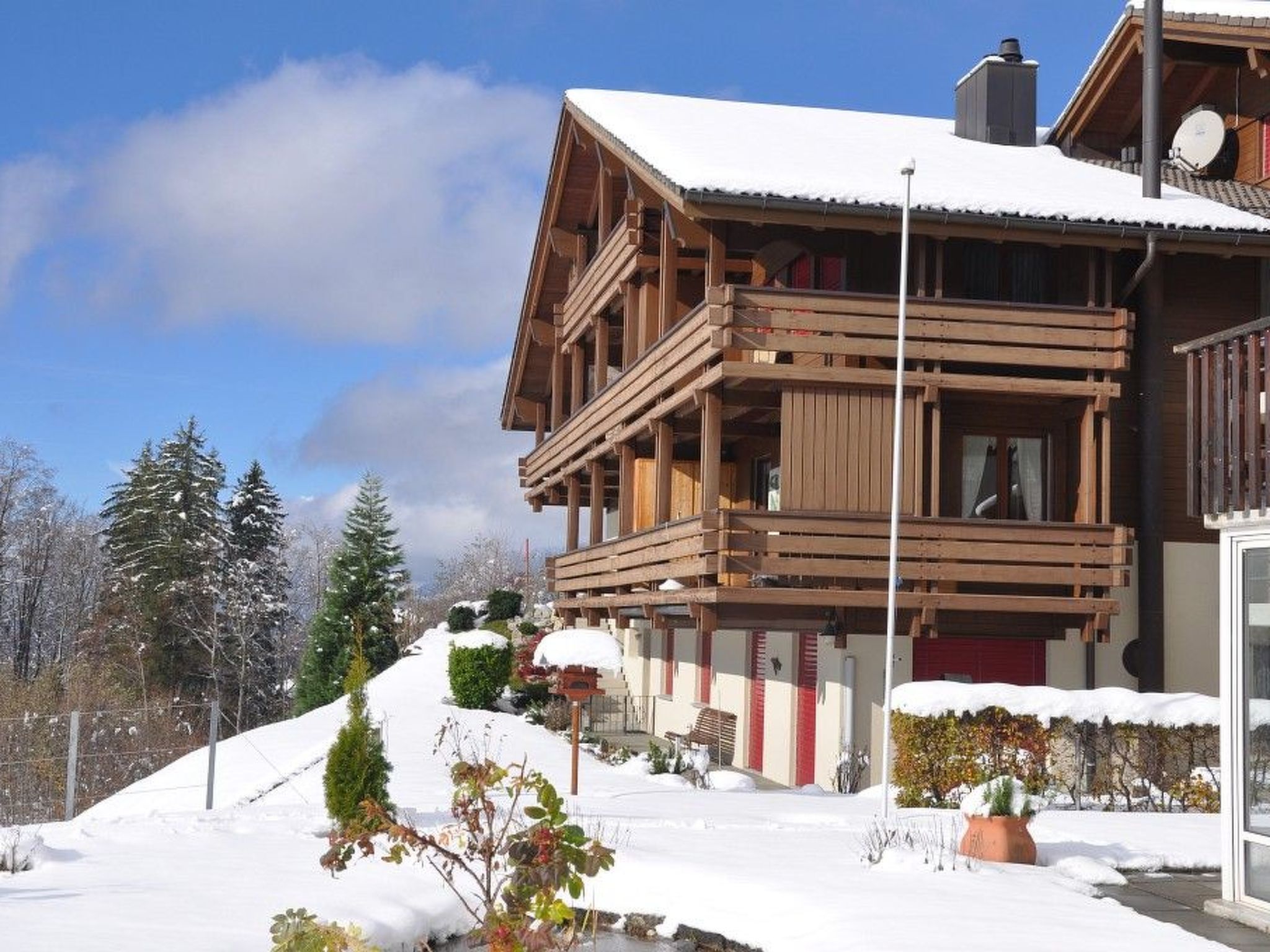 A wooden chalet with a balcony, surrounded by snow-covered trees and a clear sky.