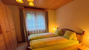 Een slaapkamer met een houten bed, een raam met gordijnen, een nachtkastje en een kledingkast.