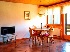 A dining area with a round table, four chairs, a television on a stand, and a window with curtains. - HasliRent, Engelhorn, (Hasliberg Reuti), by Interhome (Hasliberg)
