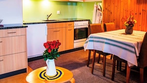A compact kitchen with wooden cabinets, a stove, and a dining area with a table and chairs. - HasliRent, Mike, (Hasliberg Reuti), by Interhome (Hasliberg)
