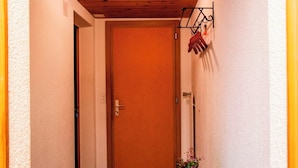 A narrow hallway with a wooden ceiling, a closed door, a hanging coat rack, and a small table with a plant. - HasliRent, Mike, (Hasliberg Reuti), by Interhome (Hasliberg)