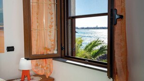 A room with a window overlooking a body of water, a wooden nightstand with a lamp, and a curtain with a leaf pattern. - Casa Vanessa by the Sea (Mandriola)
