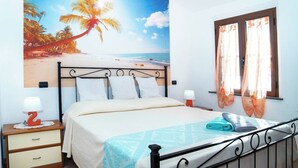 A bedroom with a bed, a nightstand, a window with curtains, and a beach-themed wall mural. - Casa Vanessa by the Sea (Mandriola)